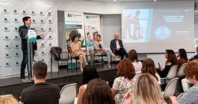 Sala en la cual se puede ver a un ponente de la jornada impartiendo su ponencia y a otros tres ponentes sentados y multitud de personas de público