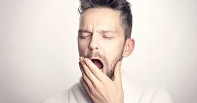 Hombre bostezando, tapándose la boca con la mano