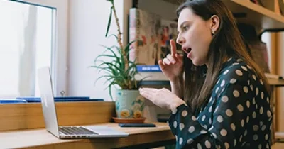 Chica delante de portátil hablando mediante lengua de signos con su interlocutor