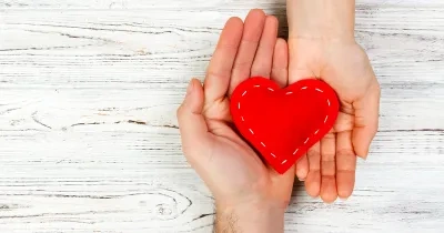 Corazón de tela roja con puntadas de hilo a su alrededor sujetado por dos manos hacia arriba