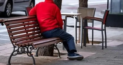Una persona mayor sola, sentada en un banco de la calle