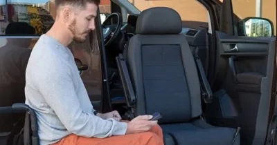 Una persona en silla de ruedas junto a un vehículo adaptado con asiento giratorio para ir de copiloto (Fuente: Rehatrans)