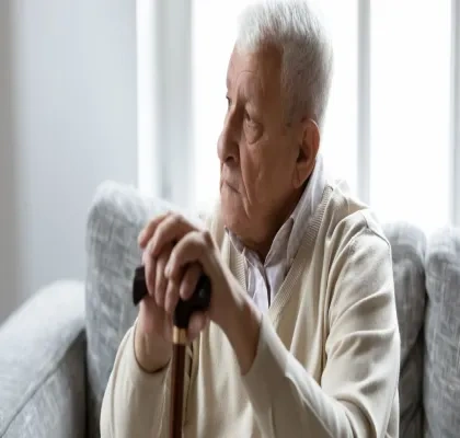 persona mayor sentada en un sofá con las manos apoyadas en una garrota