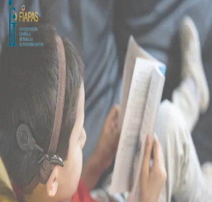 niño con discapacidad auditiva leyendo un libro en un sofça, arriba a la izquierda sale el logo de FIAPAS