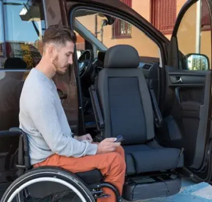 Una persona en silla de ruedas junto a un vehículo adaptado con asiento giratorio para ir de copiloto (Fuente: Rehatrans)