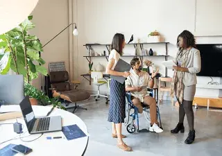 chico en silla de ruedas en la oficina hablando con dos compañeras