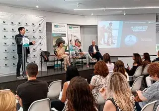 Sala en la cual se puede ver a un ponente de la jornada impartiendo su ponencia y a otros tres ponentes sentados y multitud de personas de público