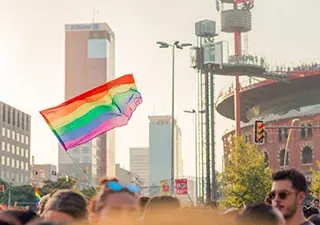 Bandera del movimiento LGTBI+ ondeando sobre multitud de personas