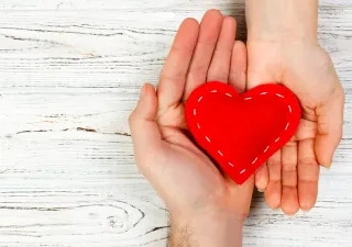 Corazón de tela roja con puntadas de hilo a su alrededor sujetado por dos manos hacia arriba