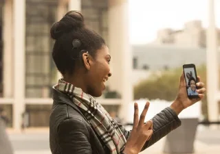 Chica con un dispositivo móvil en la mano haciendo una videollamada, hablando con lengua de signos con su interlocutor-a