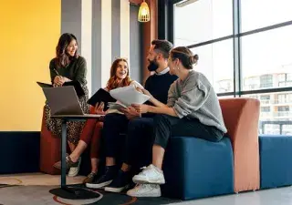 4 personas jóvenes dialogando en un sofa con un ordenador delante