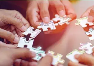 Varias manos intentando encajar un puzzle en circulo (Fuente: Servimedia)