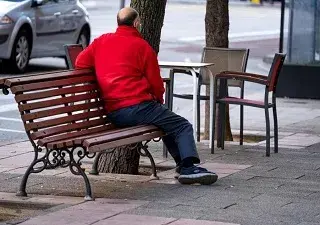 Una persona mayor sola, sentada en un banco de la calle