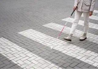 hombre con discapacidad visual andando por un paso de cebra con el baston