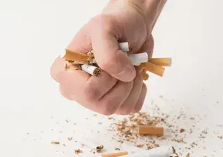 un puño cerrado con tabacos en la mano aplastándolos y rompiéndolos